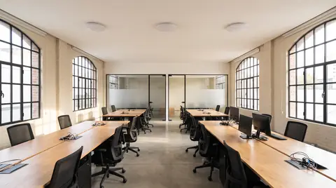 Oficina abierta para unas cuarenta personas con tres access points blancos en el techo y salas de reunión vidriadas