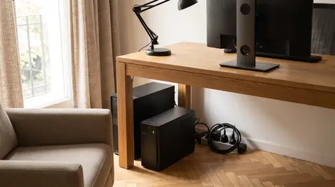 UPS de torre y una PC debajo de un escritorio de roble en un home office, con la zapatilla y los cables ordenados