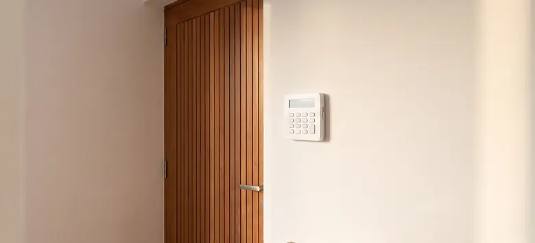 Teclado de alarma blanco instalado en la pared junto a la puerta de entrada de una casa