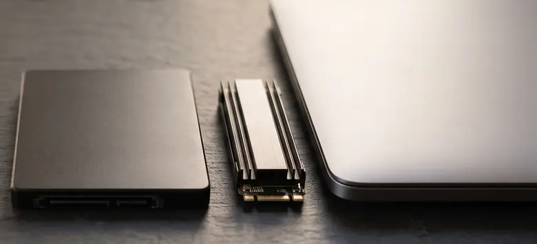 Disco SSD de 2,5 pulgadas y unidad M.2 NVMe sobre un escritorio de piedra junto a una notebook