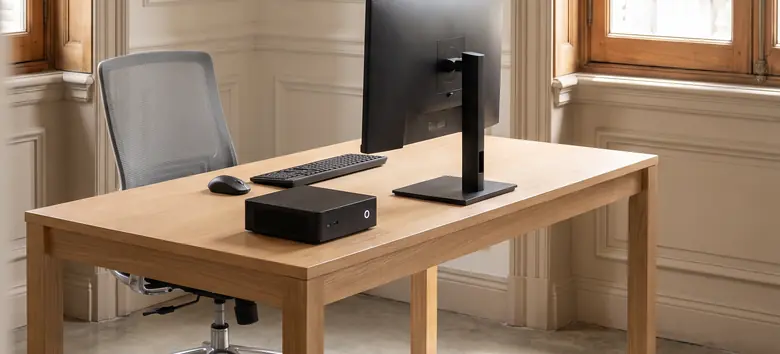 Puesto de trabajo con una mini PC negra, monitor y teclado inalámbrico sobre un escritorio de roble en una oficina de un edificio clásico de Buenos Aires