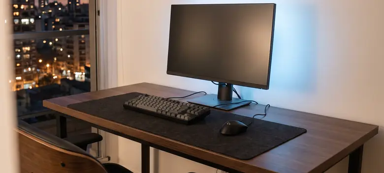 Escritorio gamer con monitor, teclado mecánico y mouse, con luz azul de ambiente y la ciudad de noche por la ventana