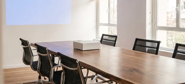 Sala de reuniones con un proyector sobre una mesa larga de nogal que proyecta un rectángulo de luz en la pared